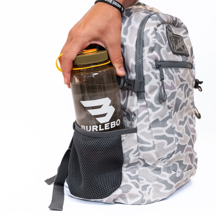 Burlebo White Camo backpack with a large insulated tumbler securely stored in the expandable side mesh pocket, demonstrating everyday carrying capacity.