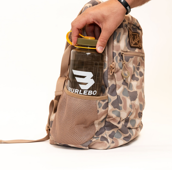 Burlebo Pintail Camo backpack with a large insulated tumbler stored securely in the side mesh pocket, demonstrating everyday carrying capacity.