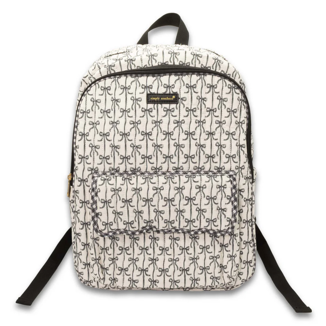 Simply Southern black bow quilted backpack featuring an allover bow print, front flap pocket, spacious zip compartment, top carry handle, and adjustable shoulder straps on a white background.