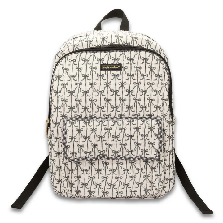 Simply Southern black bow quilted backpack featuring an allover bow print, front flap pocket, spacious zip compartment, top carry handle, and adjustable shoulder straps on a white background.