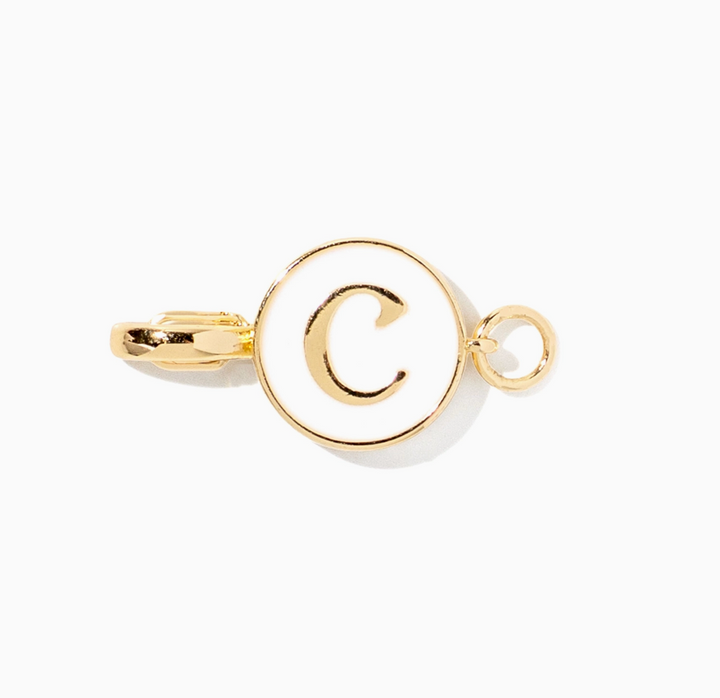 A gold-toned metal pendant charm with a circular ring and a lowercase &