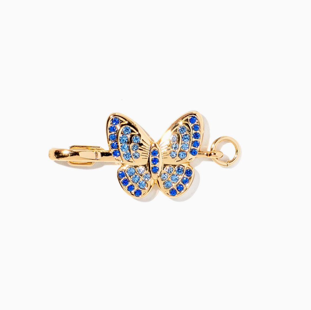 Gold butterfly pendant charm embellished with blue and clear rhinestones, shown on a plain white background.
