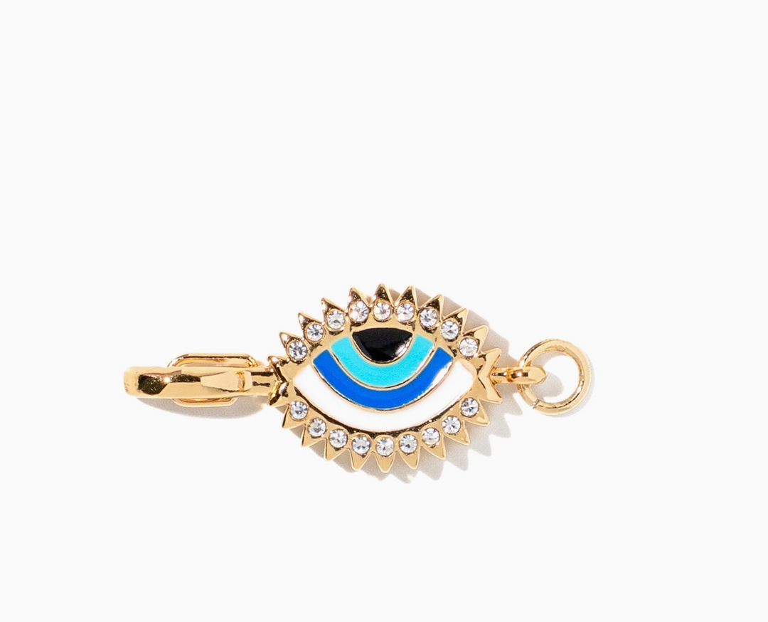 Gold evil eye charm with blue and black enamel, accented with small clear rhinestones, on a white background.