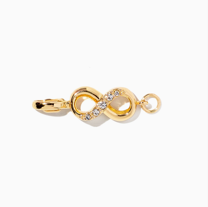 A gold infinity symbol charm decorated with small clear crystals along the center, featuring a lobster clasp on one end and a small ring on the other, set against a plain white background.