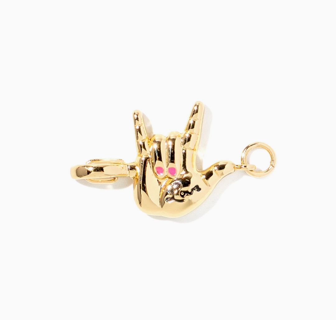 A gold charm shaped like a hand making the shaka sign, featuring small pink and clear rhinestone eyes, shown on a plain white background.