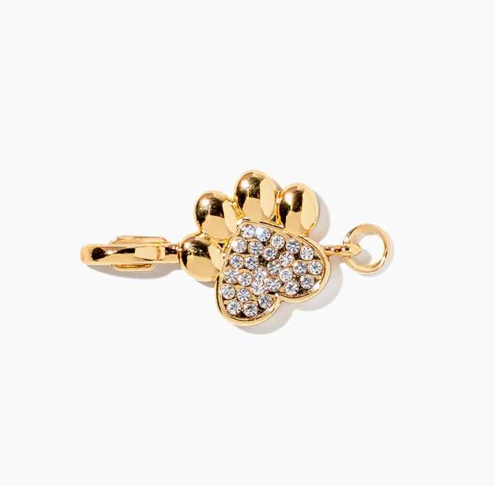 A gold-toned pet pendant charm shaped like a paw print, featuring a heart-shaped pad decorated with clear pavé stones, shown on a clean white background.
