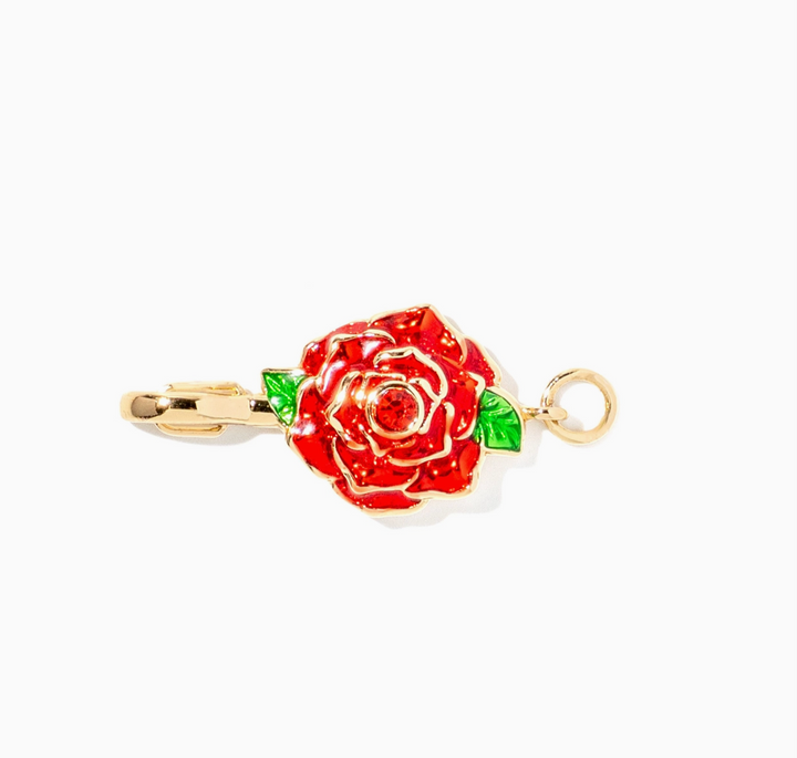 A gold-tone rose-shaped pendant charm with red enamel petals and small green leaf accents, shown on a plain white background.