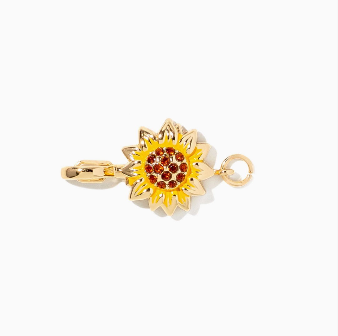 A gold-toned sunflower charm with a yellow enamel center and small red gemstone accents, shown on a plain white background.