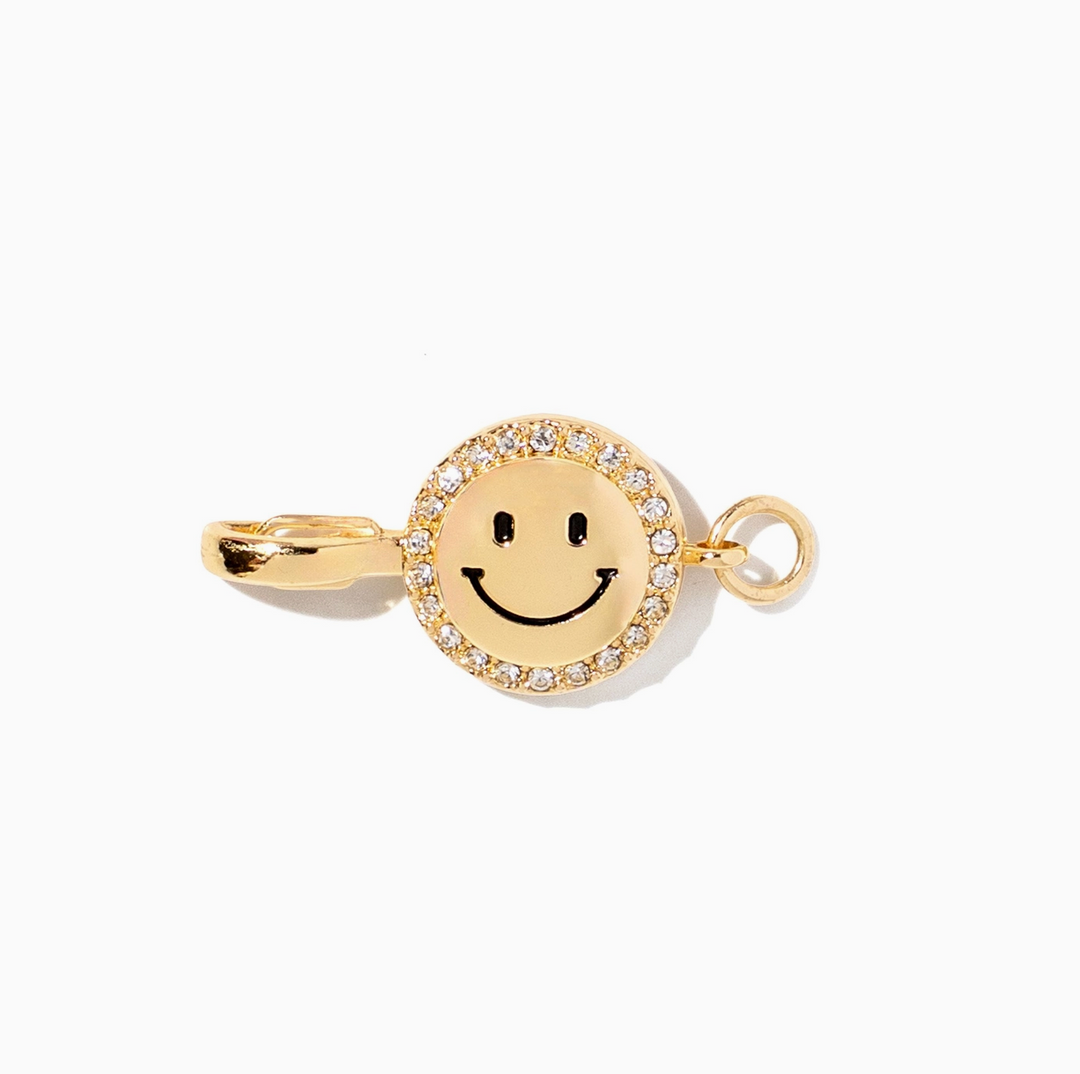 A gold smiley face charm with a halo of clear rhinestones, shown on a clean white background.