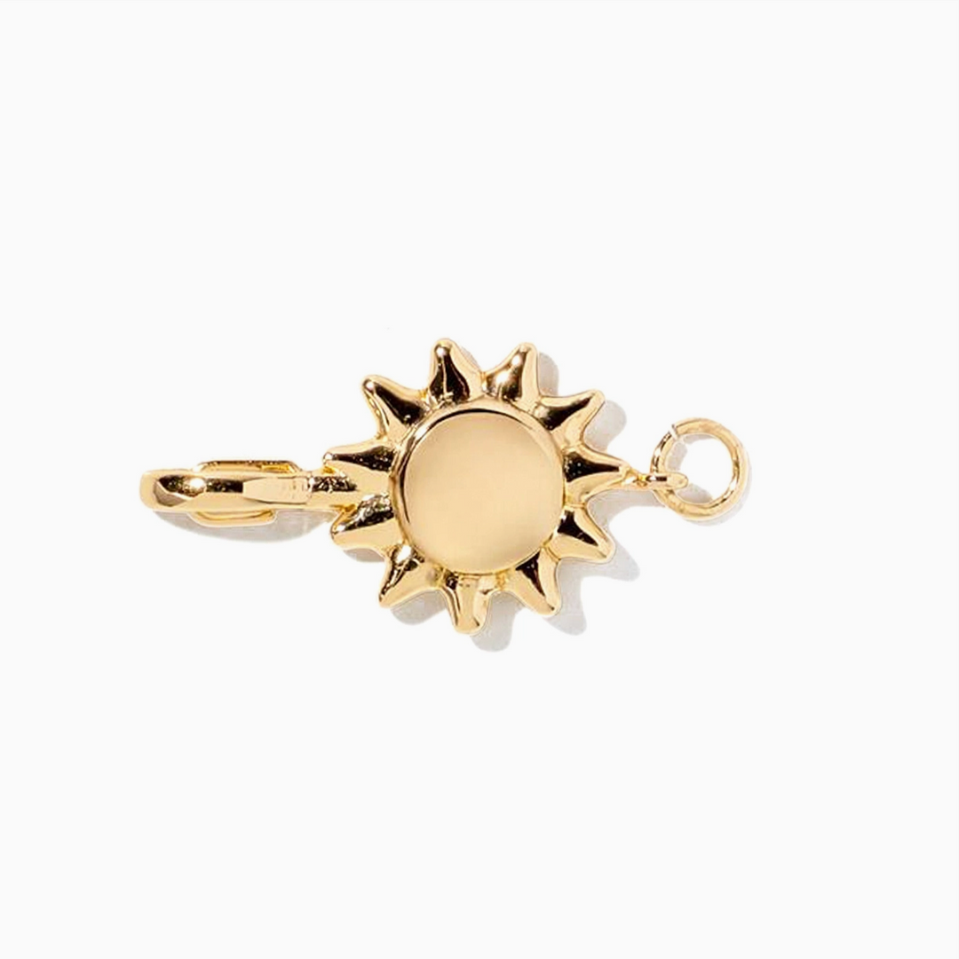A gold-toned metal charm shaped like a sun with a flat circular center and pointed rays, shown on a plain white background.
