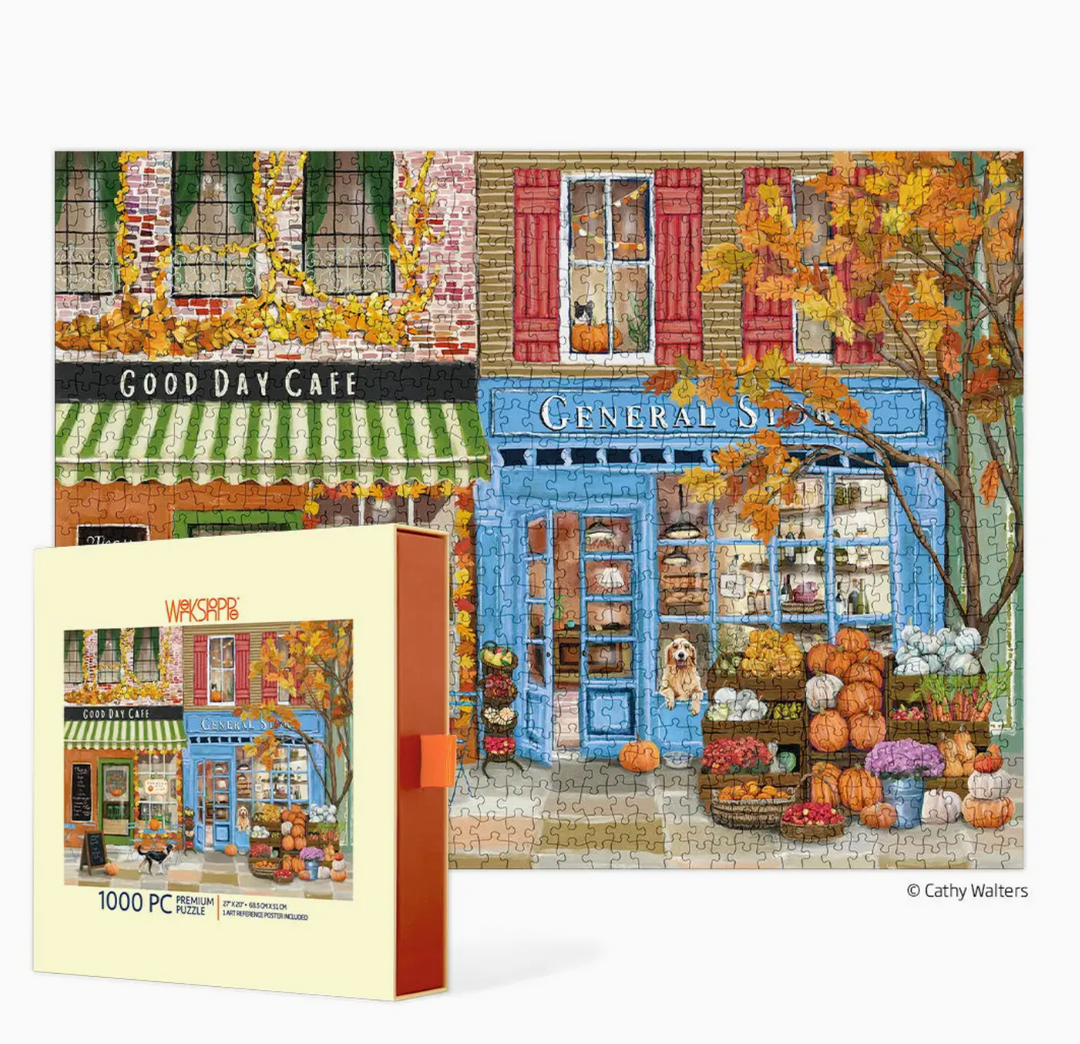 A 1000-piece jigsaw puzzle box shown alongside the completed puzzle, featuring an autumn street scene with storefronts, pumpkins, and colorful buildings. The box reads &