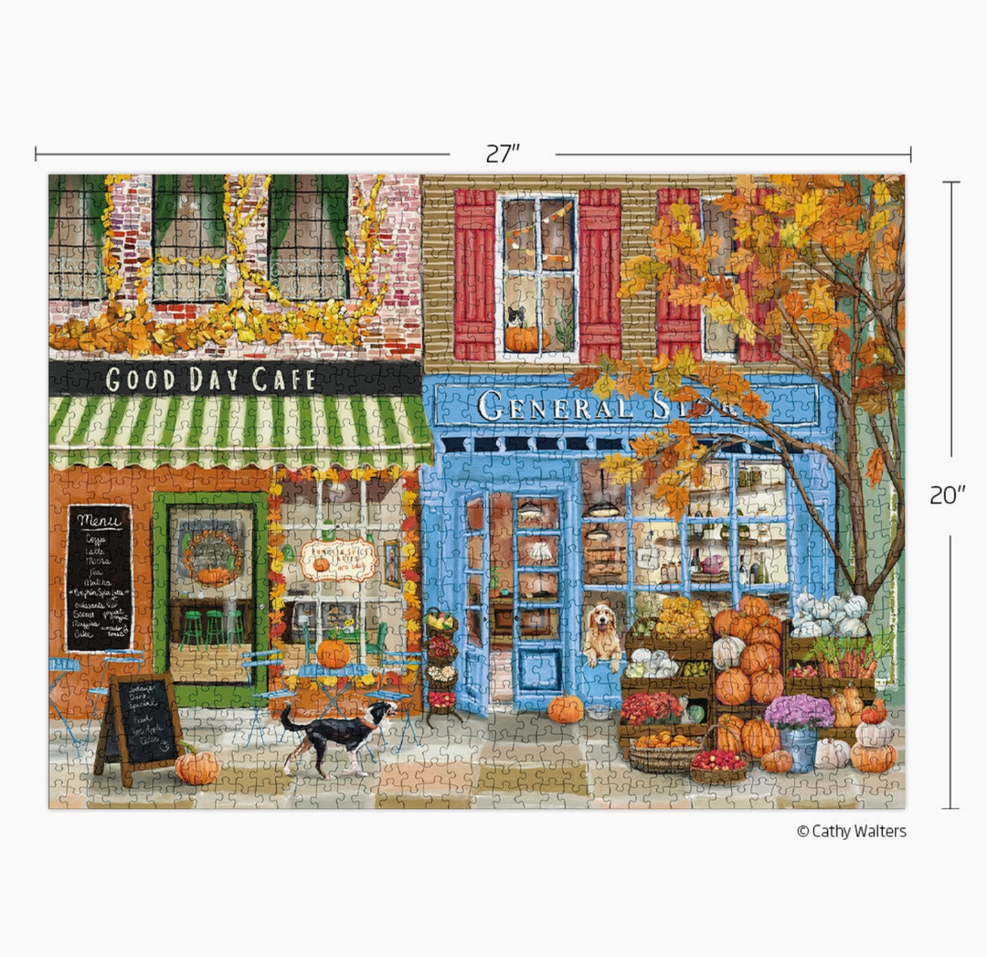 A completed jigsaw puzzle showing a colorful autumn street scene with two storefronts, one green and white striped and one blue, decorated with pumpkins, fall leaves, and flowers. White measurement lines with 27" and 20" labels indicate the puzzle dimensions.