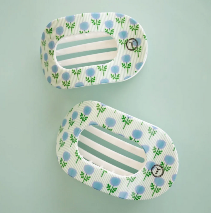Two matching hair claw clips with a white and light blue striped pattern, decorated with small blue flowers and green stems, shown on a pale mint green background.