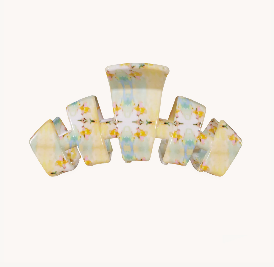 A curved hair claw clip with a glossy finish, decorated with a delicate pastel floral pattern in soft yellow, blue, and green on a white base, set against a plain off-white background.