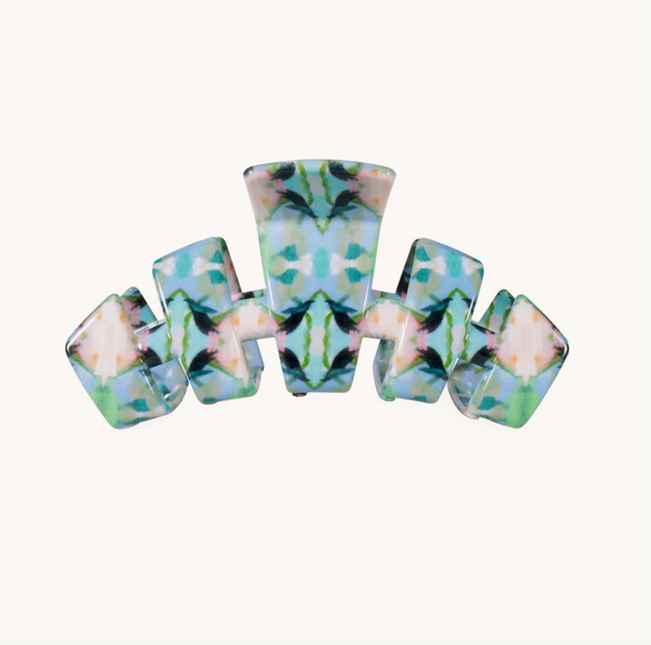 A symmetrical hair claw clip made of glossy resin with a marbled pattern of light blue, mint green, beige, and black swirls, shown on a plain off-white background.