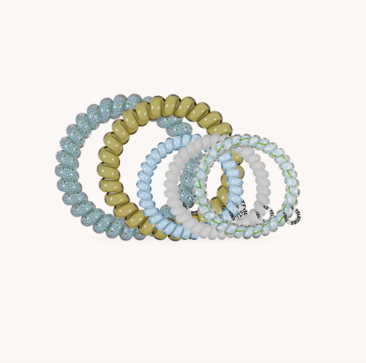 Five beaded stretch hair ties in pastel shades of light blue, sage green, white, and pale yellow, arranged in a fan shape on a light cream background.