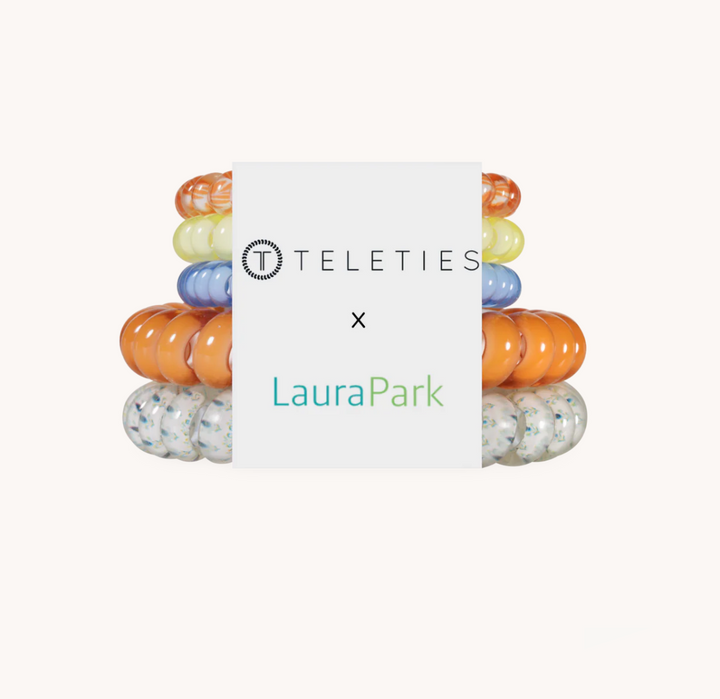 A product bundle of silicone baby teething rings from Teleties and LauraPark, featuring a central white card with the brand logos and a stack of colorful rings behind it on a light beige background.