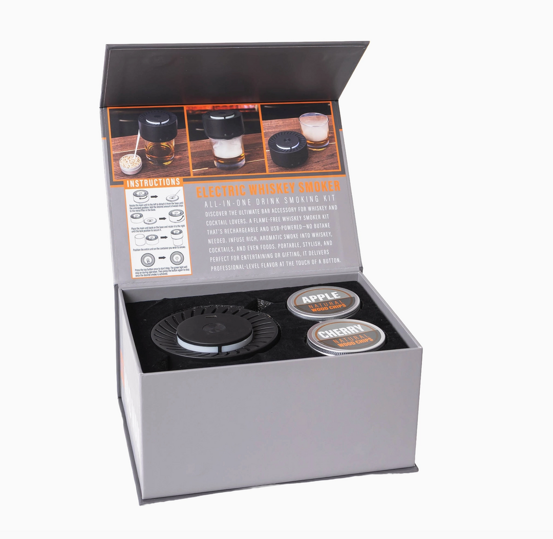 An open gray presentation box containing a whiskey stone set, including a black circular stone and two round tin containers labeled Apple and Cherry, with an instruction insert inside the lid.