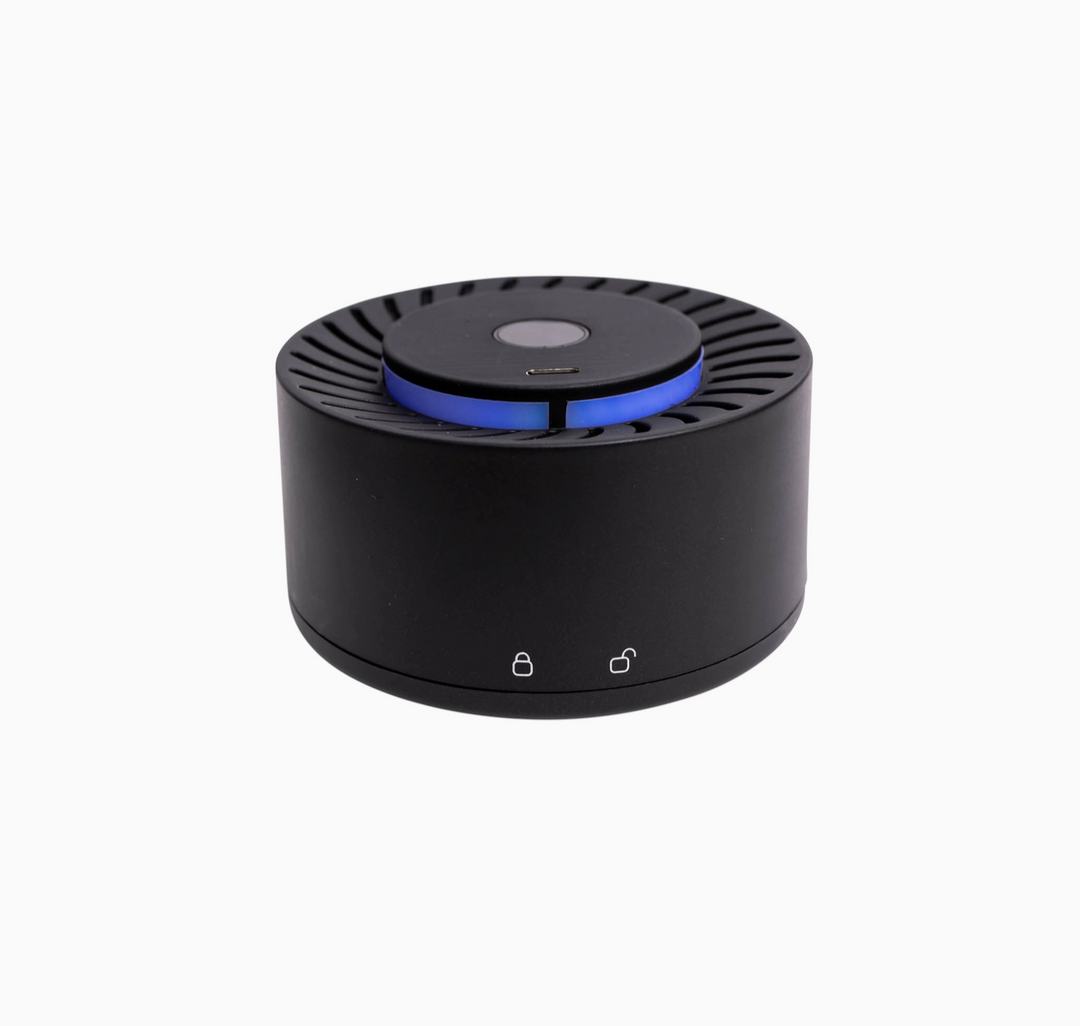 A black cylindrical electronic device, likely a portable speaker or air freshener diffuser, featuring a blue illuminated ring around the top center and two small white icons on the front base, shown against a plain white background.