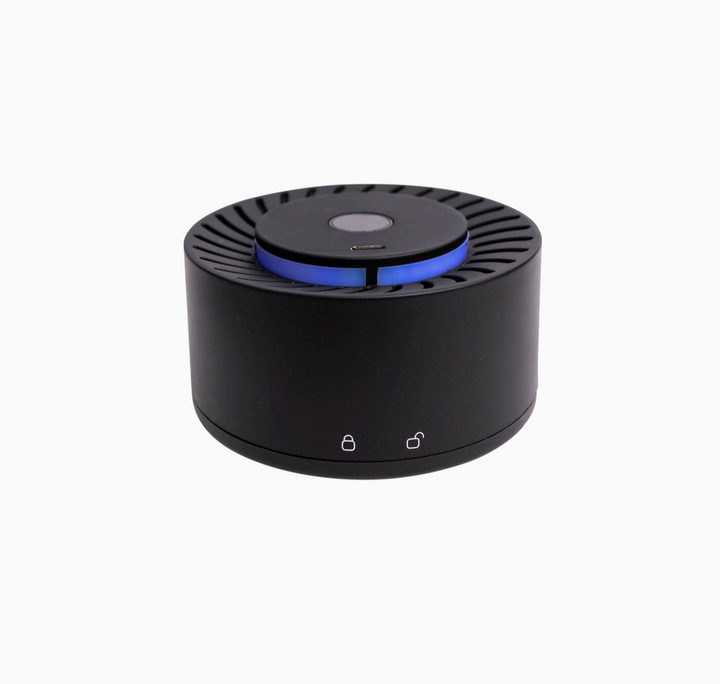 A black cylindrical electronic device, likely a portable speaker or air freshener diffuser, featuring a blue illuminated ring around the top center and two small white icons on the front base, shown against a plain white background.