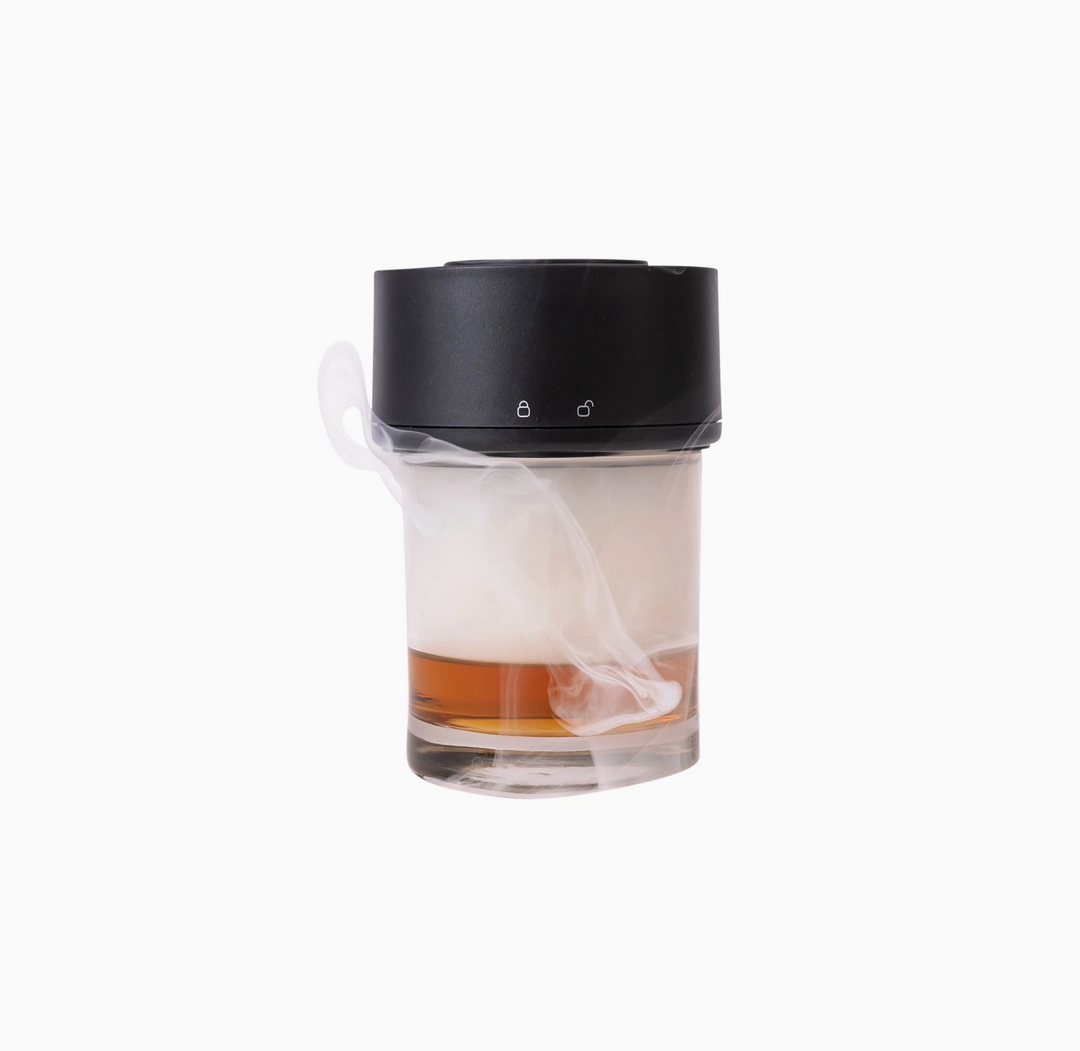 A portable glass diffuser with a black lid and a clear glass body containing amber liquid, with white wax melts or vapor visibly diffusing, on a plain white background.
