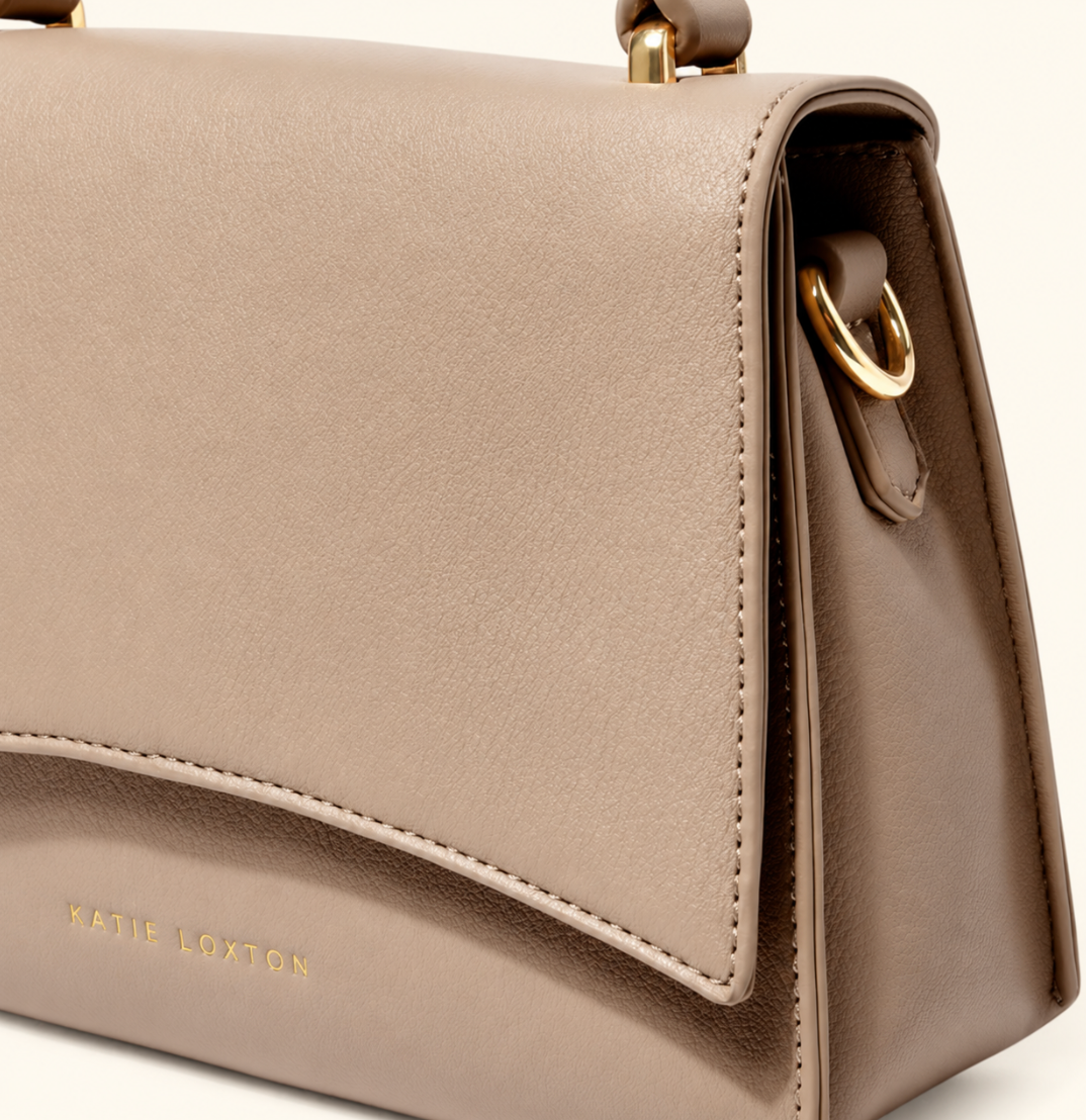 Close-up of Katie Loxton Rae Crossbody Bag in Soft Tan showing the curved flap, gold Katie Loxton logo, stitching, and side hardware.