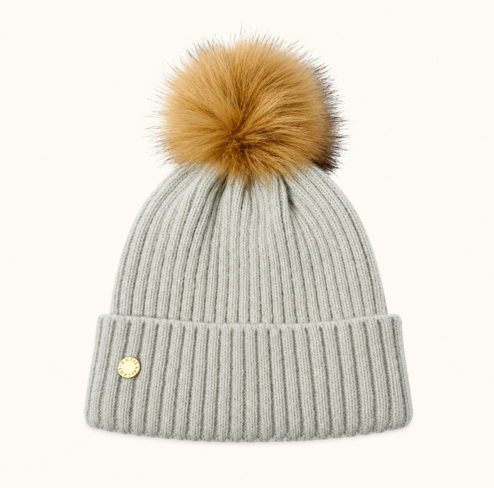 Katie Loxton Knitted Hat in Cool Grey with ribbed knit design, folded cuff, gold logo charm, and tan faux fur pom pom.