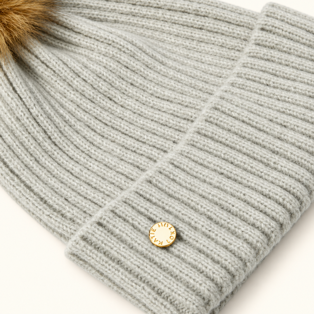 Close-up of Katie Loxton Cool Grey Knitted Hat showing soft ribbed knit texture, folded cuff, and gold Katie Loxton logo charm.