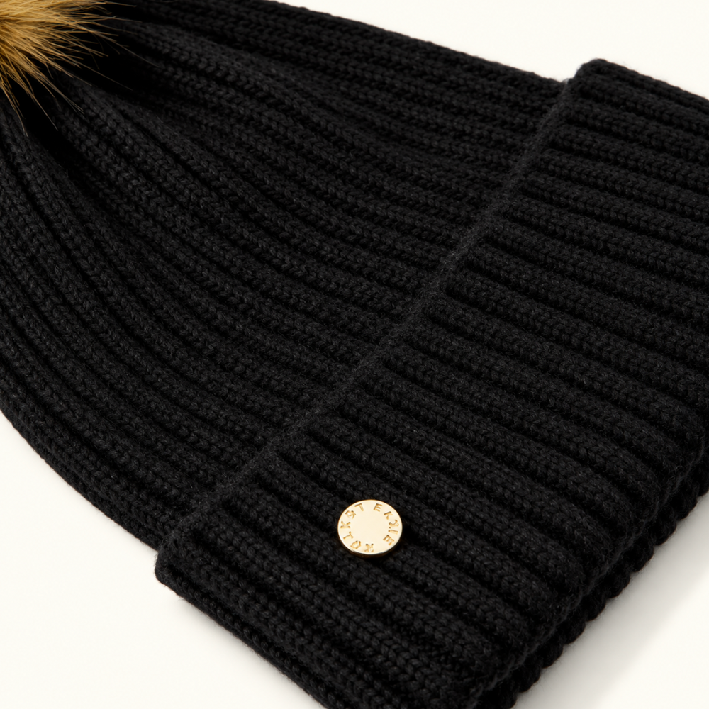 Close-up of Katie Loxton Black Knitted Hat showing chunky ribbed knit texture, folded cuff, and gold Katie Loxton logo charm.