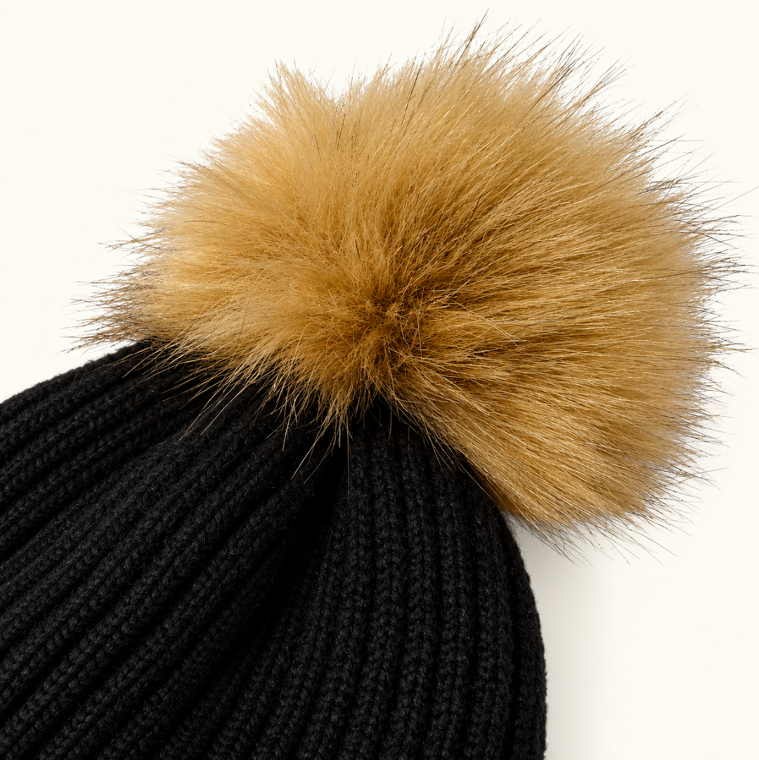 Close-up of Katie Loxton Black Knitted Hat featuring the fluffy tan faux fur pom pom and textured black ribbed knit.