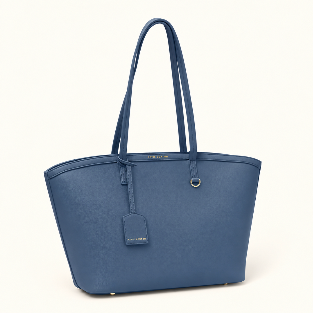 Angled front view of Katie Loxton Travel Tote in Navy with spacious structured design, long shoulder handles, luggage tag, and gold-tone accents.