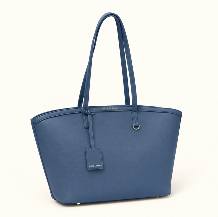 Angled front view of Katie Loxton Travel Tote in Navy with spacious structured design, long shoulder handles, luggage tag, and gold-tone accents.