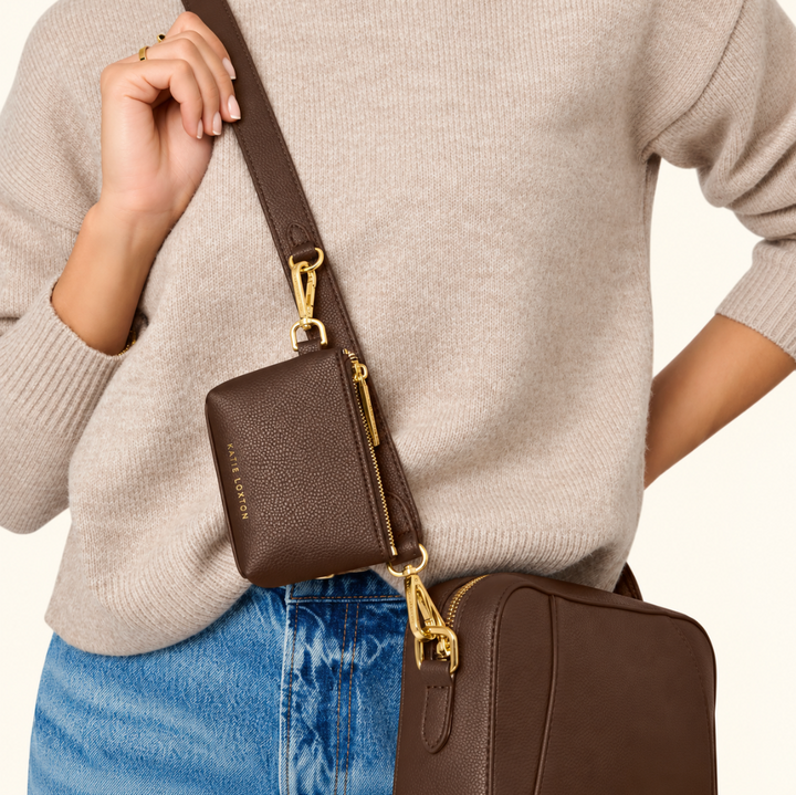 Katie Loxton Evie Clip-On Coin Purse in Chocolate attached to a brown crossbody bag strap with gold hardware for hands-free everyday use.