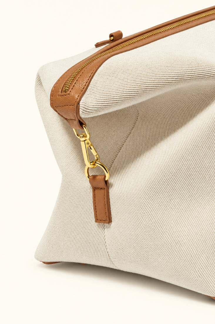 Close-up side view of Katie Loxton Capri Canvas Weekender Bag showing off white canvas, tan vegan leather trim and gold strap hardware