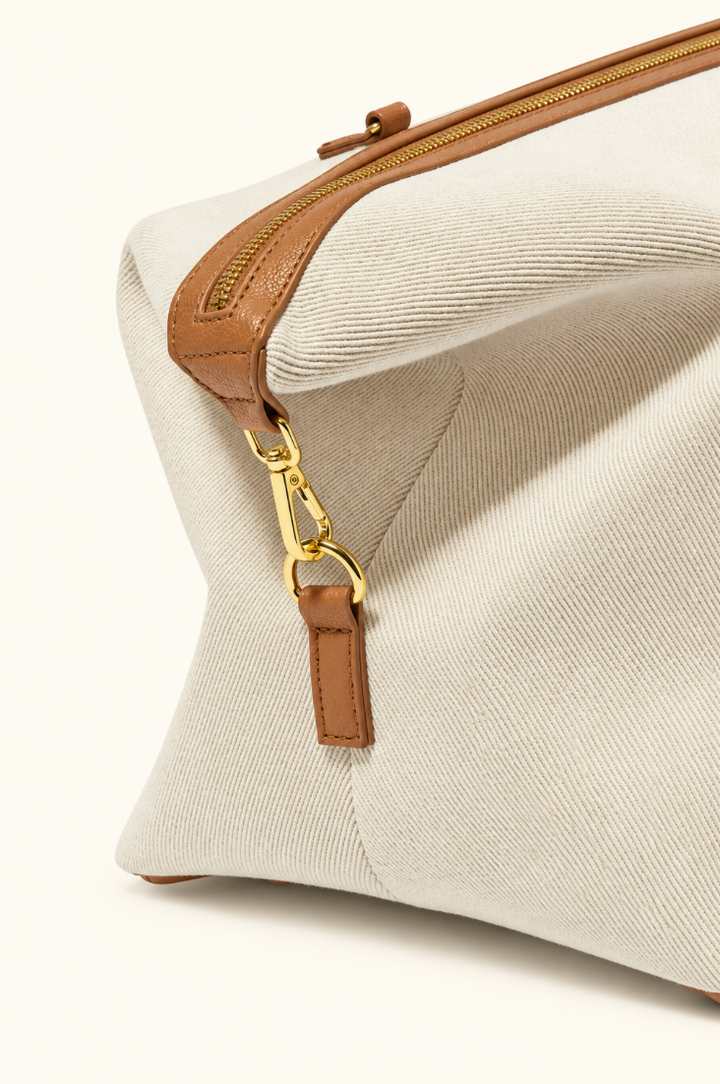 Close-up side view of Katie Loxton Capri Canvas Weekender Bag showing off white canvas, tan vegan leather trim and gold strap hardware