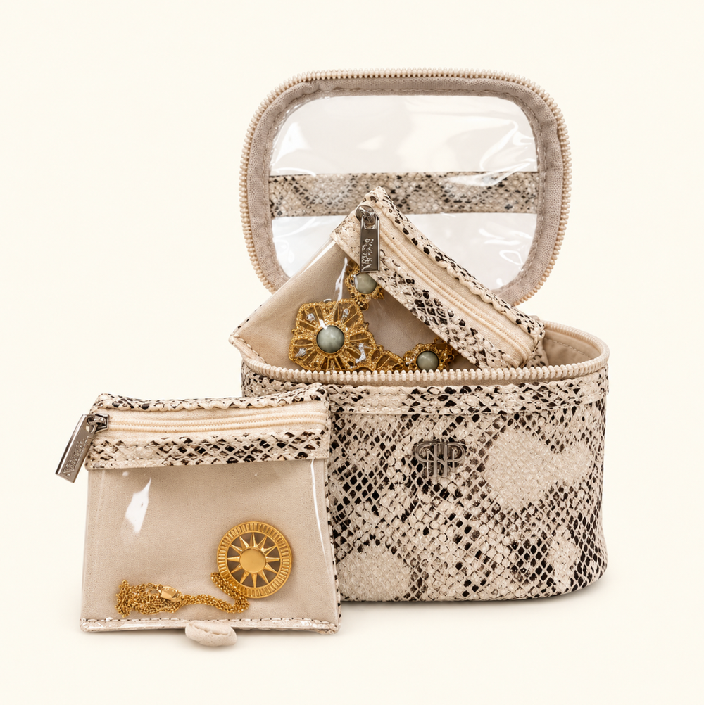 Safari Sands cream snakeskin print jewelry organizer with clear-view lid, removable jewelry pouches, and gold statement earrings displayed on a cream background.