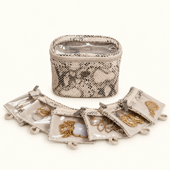 Safari Sands jewelry travel case with six removable clear-front pouches displaying gold necklaces, rings, earrings, and other jewelry on a cream studio background.