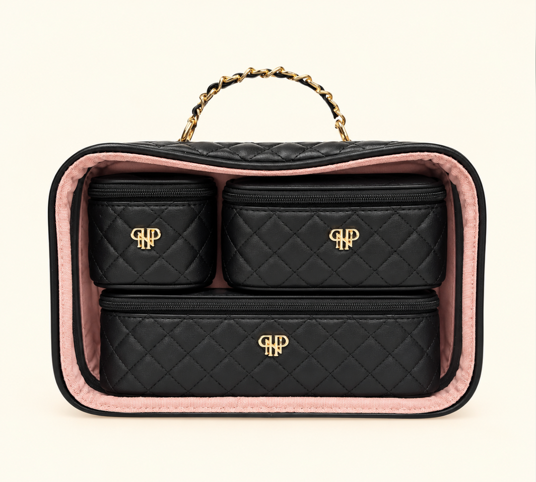Black quilted makeup organizer set featuring three matching zippered cosmetic bags with gold monogram accents, displayed inside a clear travel case with blush pink lining and gold chain handle on a cream background.