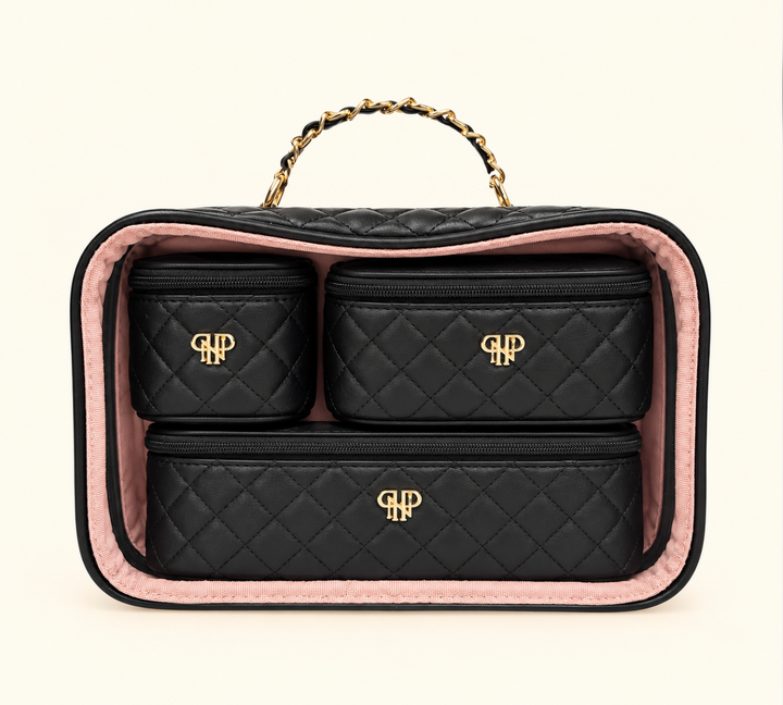 Black quilted makeup organizer set featuring three matching zippered cosmetic bags with gold monogram accents, displayed inside a clear travel case with blush pink lining and gold chain handle on a cream background.