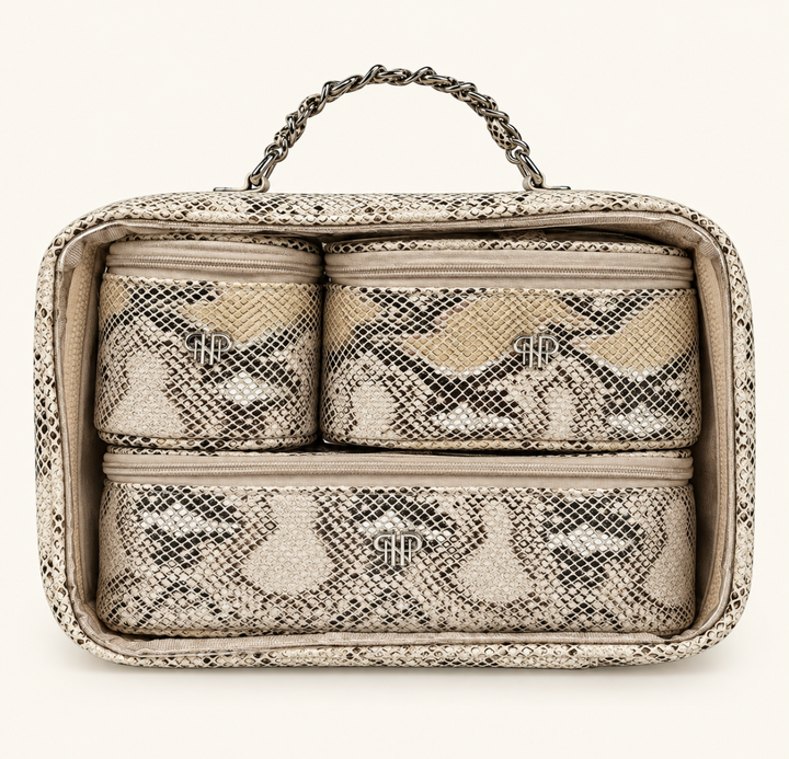 Snakeskin print makeup travel organizer set featuring three matching zippered cosmetic bags neatly packed inside a clear carrying case with silver chain handle.