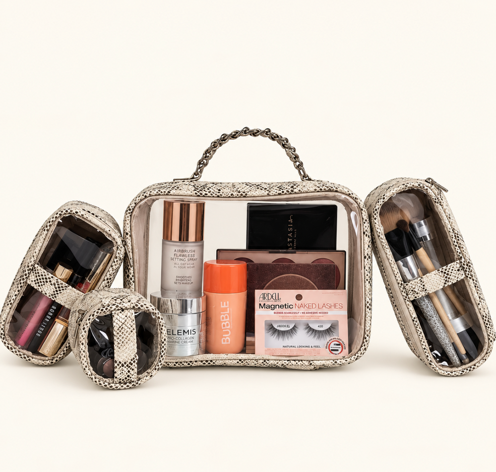 Snakeskin print four-piece makeup travel organizer set featuring clear cosmetic bags filled with makeup, beauty essentials, and brushes on a cream background.
