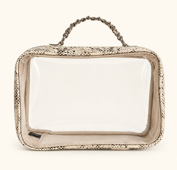 Empty clear makeup travel organizer case with beige snakeskin print trim, silver chain handle, and zippered closure on a cream background.