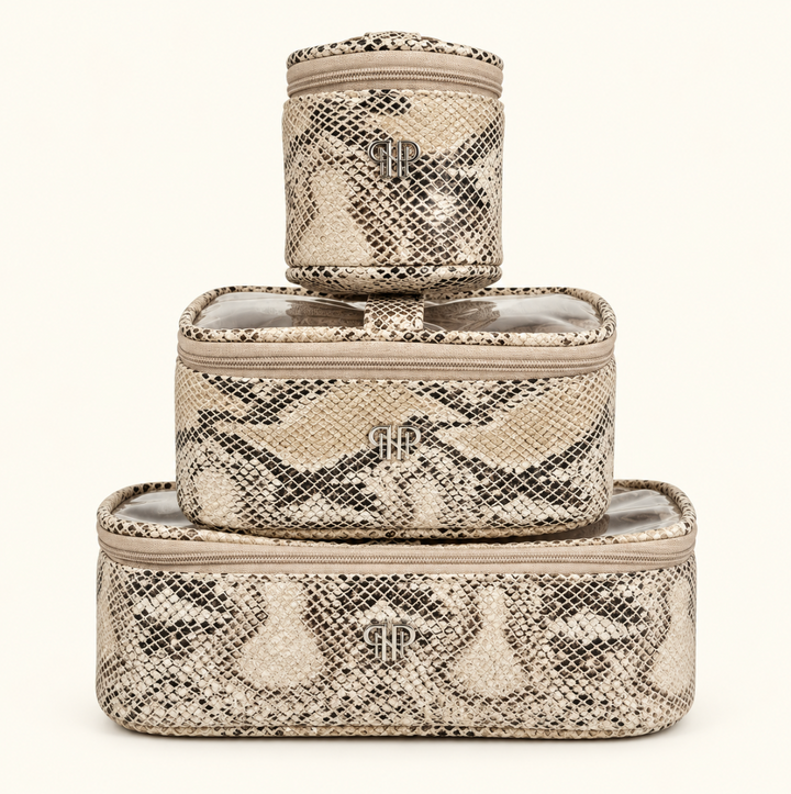 Three matching snakeskin print cosmetic organizer bags stacked by size, featuring beige zippered closures and silver logo accents on a cream background.