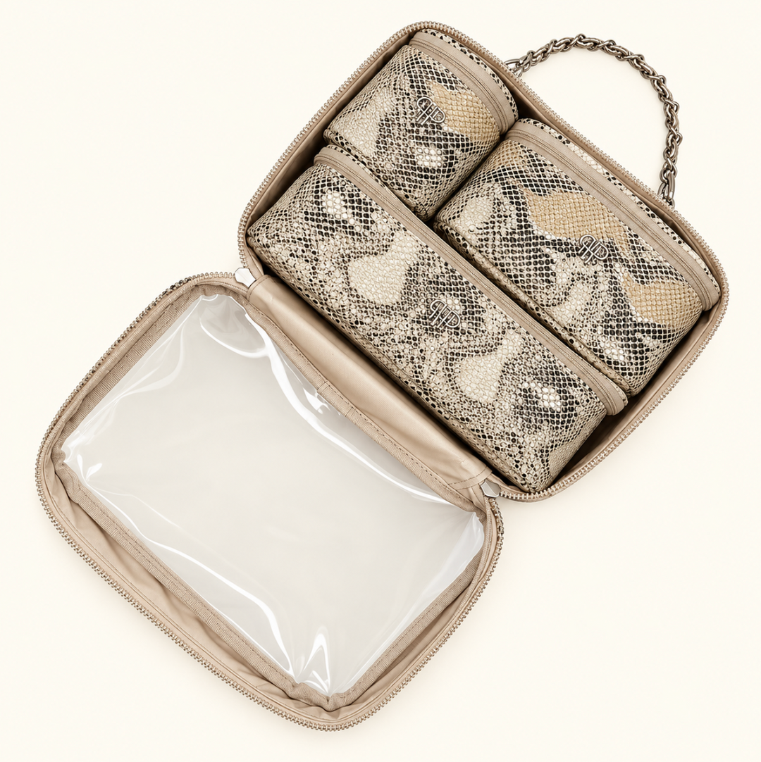 Overhead view of an open snakeskin print makeup travel organizer featuring three removable zippered cosmetic pouches, clear interior compartment, and silver chain handle on a cream background.