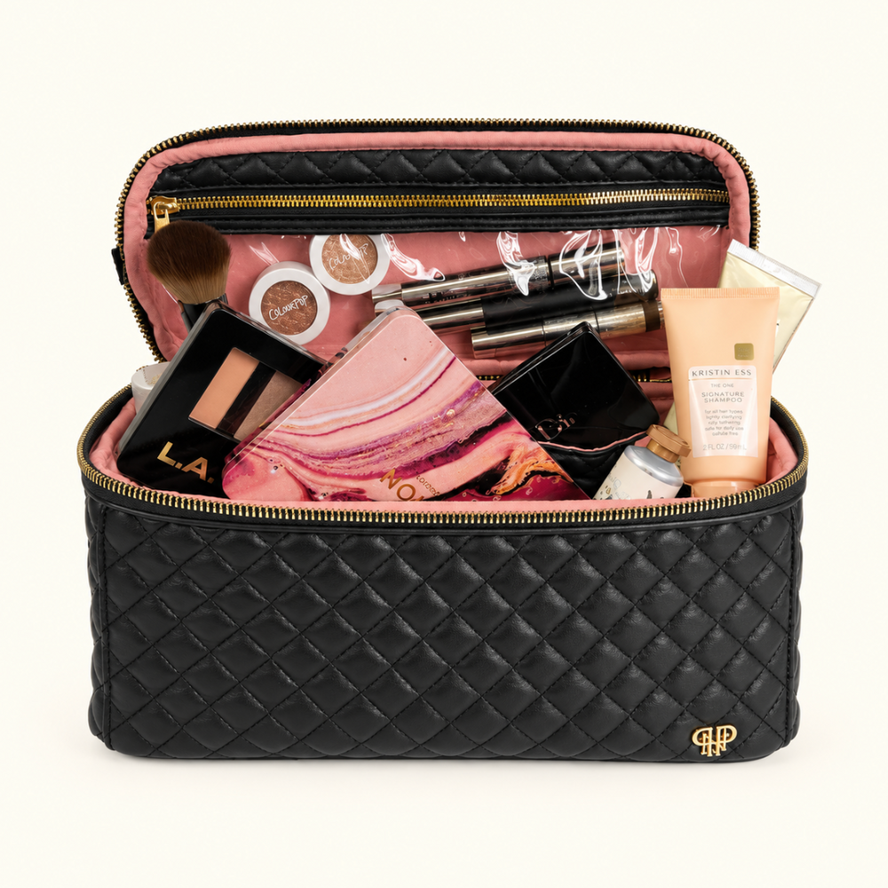 Open black quilted cosmetic travel bag with blush pink interior, clear zippered pocket, gold hardware, and spacious storage for makeup, skincare, and beauty essentials.