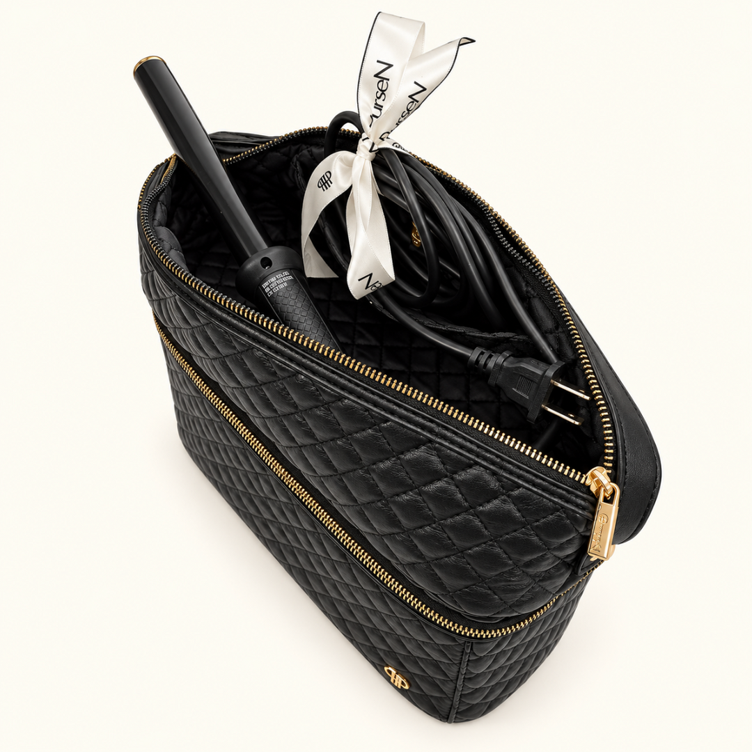Black quilted travel organizer with heat-resistant compartment holding a curling iron and power cord, featuring gold zippers and a cream studio background.