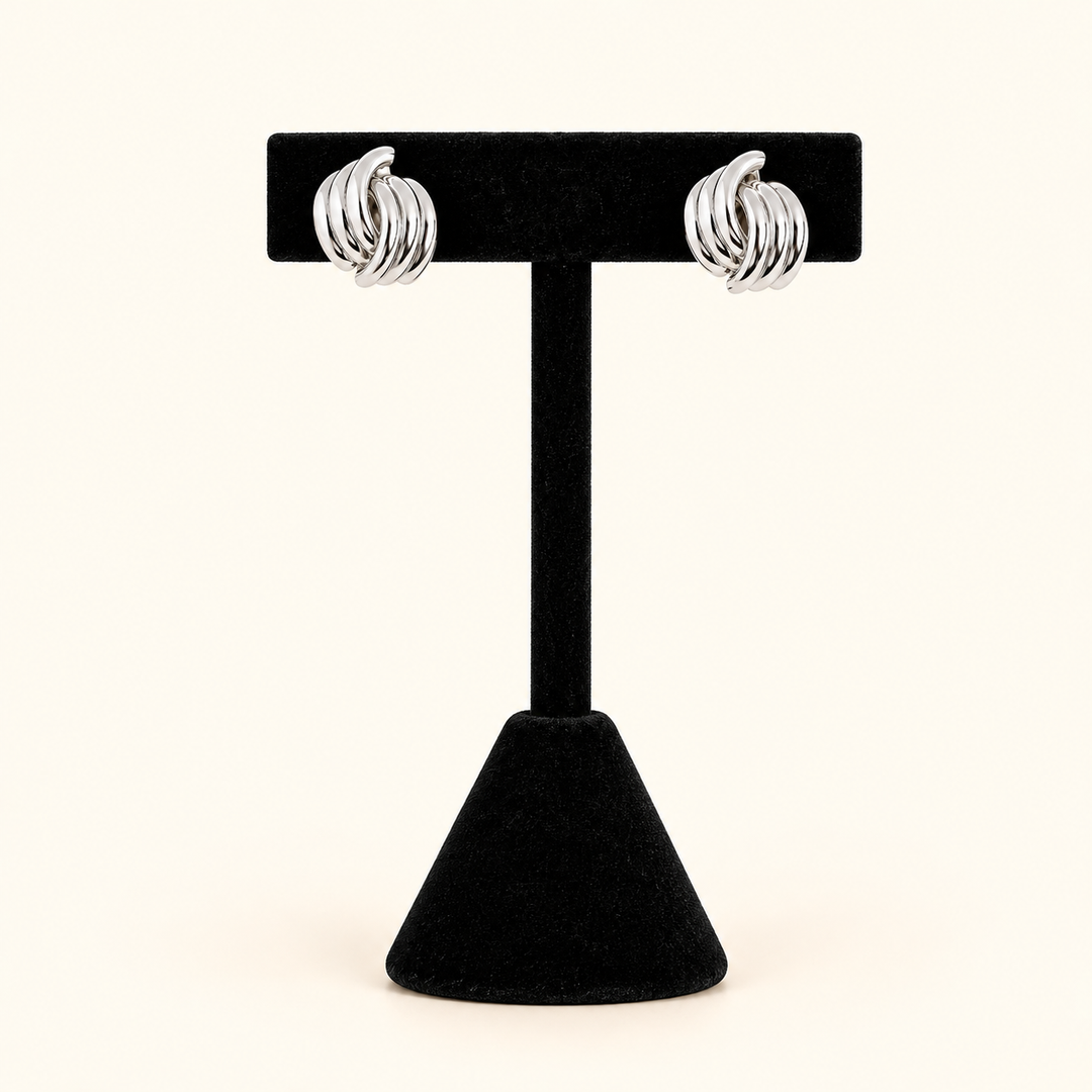 0.5-inch silver-tone knot hoop earrings with intertwined, high-shine metal bands displayed on a black velvet T-bar jewelry stand against a cream background.