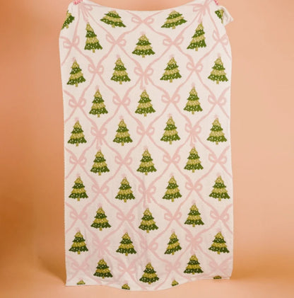 blanket with green Christmas tree and pink bow pattern on a peach background