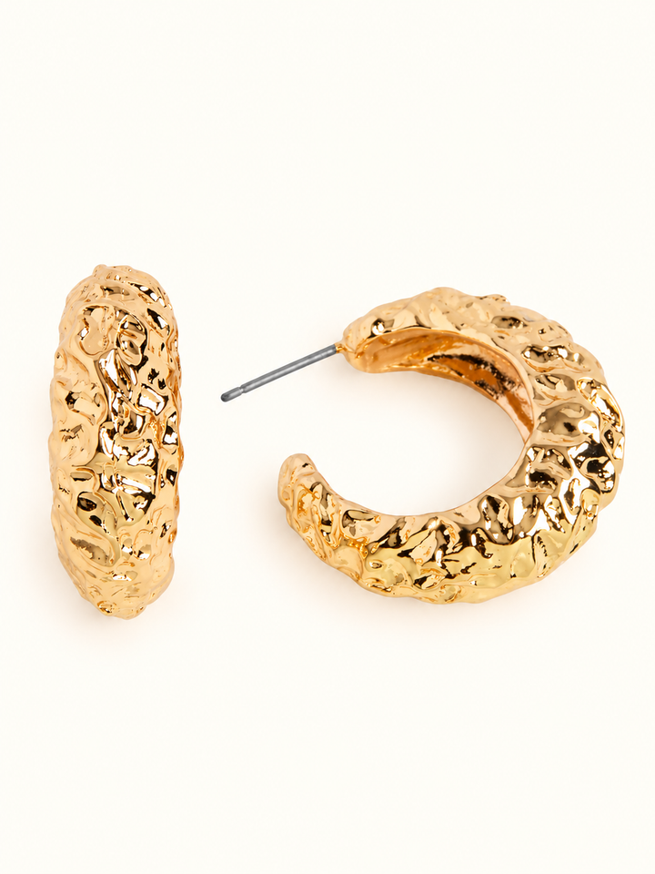 1-inch chunky gold-tone hammered hoop earrings featuring a textured, sculpted C-shaped design with post closures on a cream background.