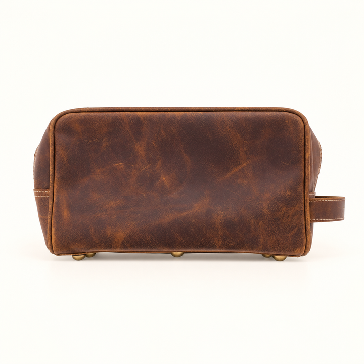 Full bottom view of the Dusty Dopp Kit brown leather travel toiletry bag showing its vintage-inspired leather texture, reinforced edges, and brass-tone feet.